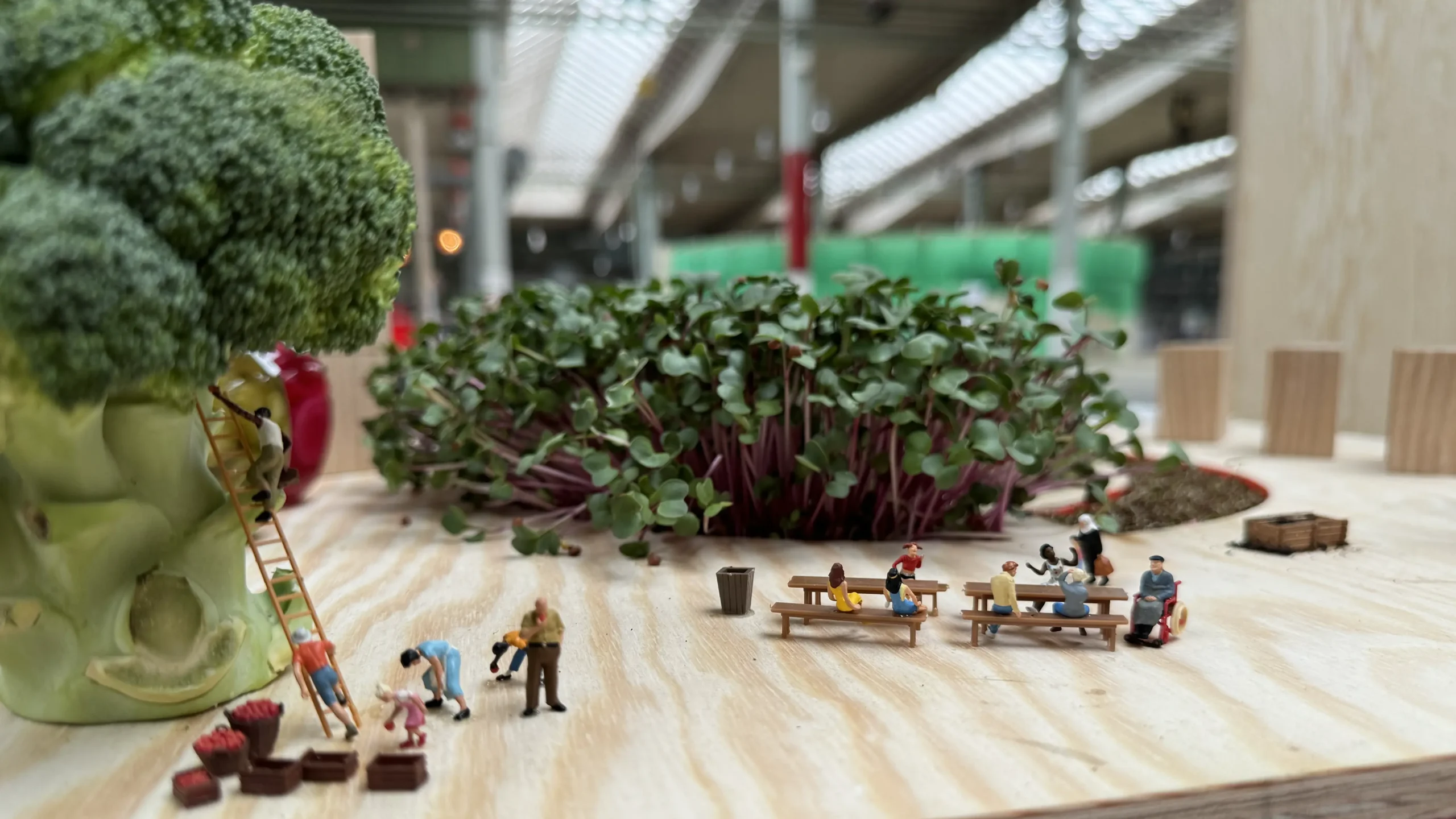 Tiny people climbing a giant broccoli and sharing a meal at long tables in Rosengård